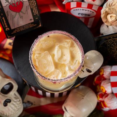 Passion for Passion cocktail in a rocks glass, surrounded by Halloween decorations.