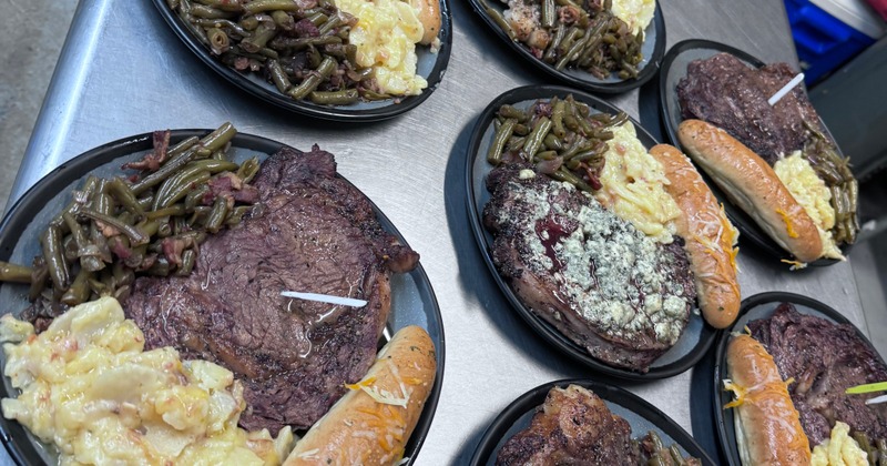 Several servings of ribeye steaks with sides on a kitchen counter