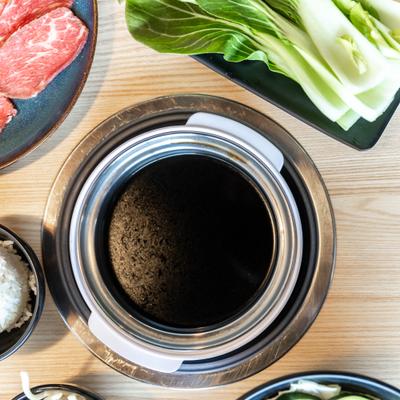 Dark broth in a pot, salad leaves, top view, closeup.