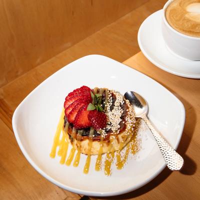 Dessert topped with sliced strawberries and sauce beside a cup of coffee.