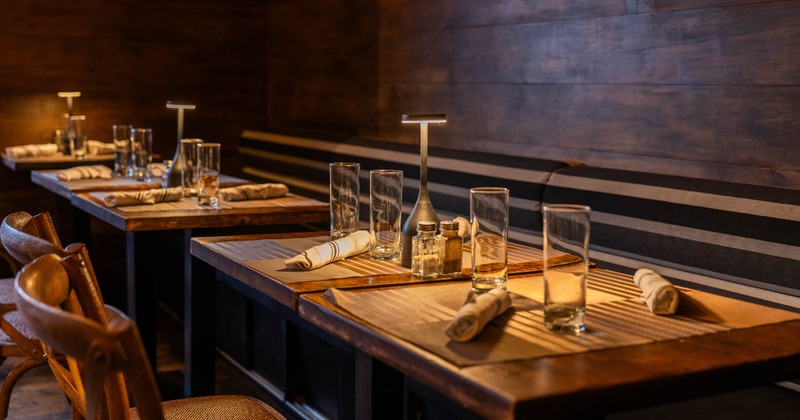 Interior, wooden tables, glassware, napkins, condiments, dark wood walls, striped bench
