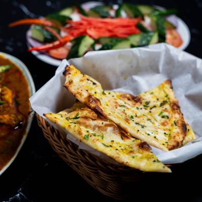Naan pieces in a wicker basket and surrounding dishes.