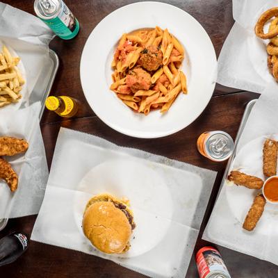 Pasta with meatballs, cheeseburger, mozzarella sticks, fries and drinks on the table.