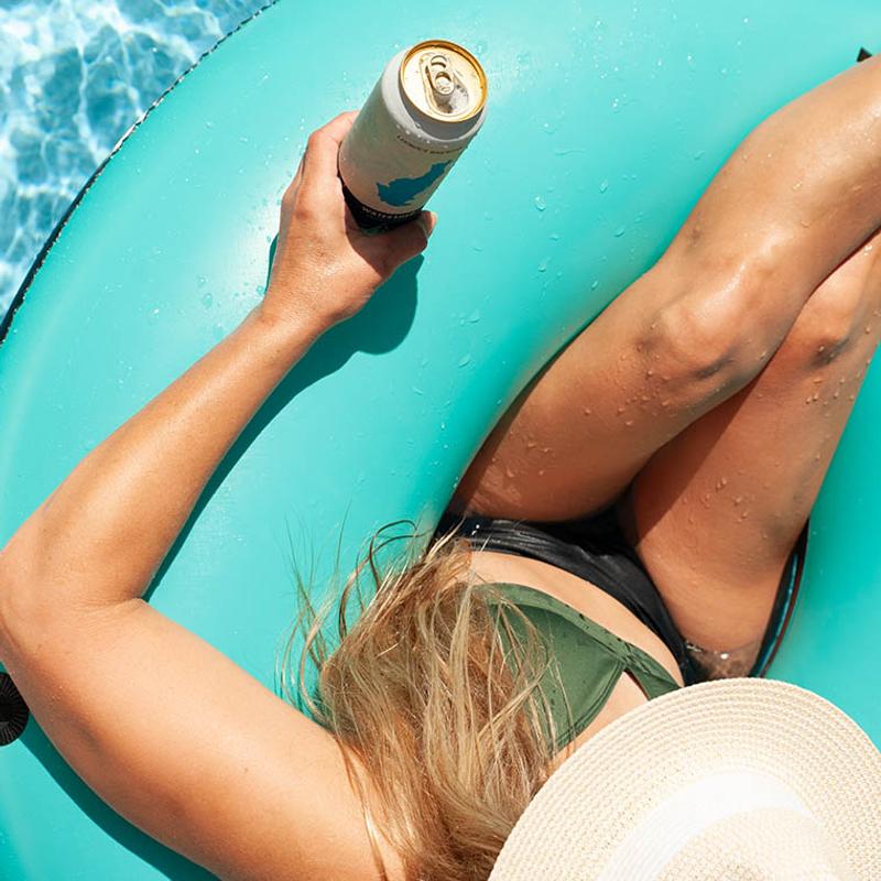 Person lounging on a teal-colored inflatable pool float while holding a beer can.