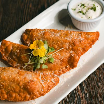 Empanadas garnished with microgreens and a yellow edible flower, served with a dip.