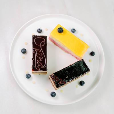 Three rectangular pastries on a white plate with decorative blueberries and sauce droplets.