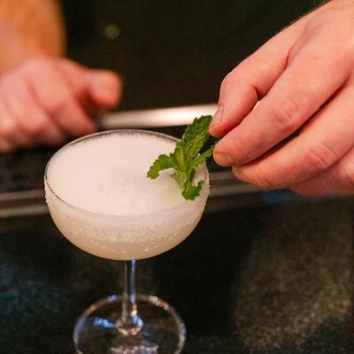 A bartender finishes a hazy white cocktail with mint leaf garnish.