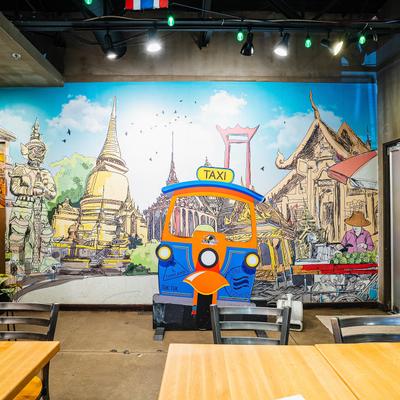 Thai restaurant interior featuring a colorful mural of Bangkok landmarks and a blue tuk-tuk.