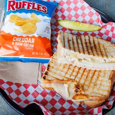 Brie & Pears hot panini with a bag of chips and a pickle spear.