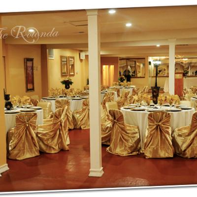 Banquet hall featuring white tables and chairs with gold satin covers.