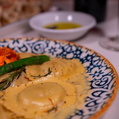 Ravioli in saffron cream sauce garnished with a grilled asparagus spear and a flower.