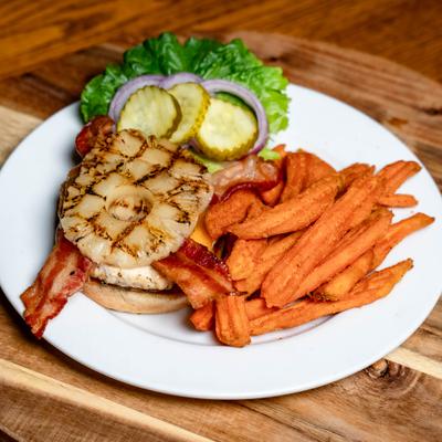 Chicken sandwich topped with bacon and a grilled pineapple slice, served with sweet potato fries.