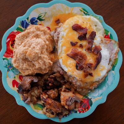 A colorful plate featuring cheesy eggs topped with bacon, creamy grits, and crispy smashed potatoes.