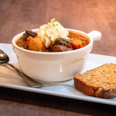 A serving of hearty beef stew with mashed potatoes served with a slice of brown bread.
