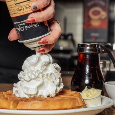 Waffle being topped with whipped cream.