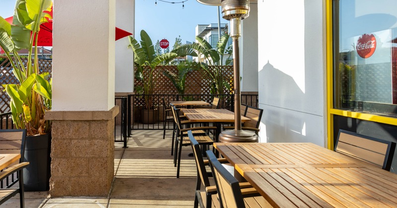 Outdoor patio with wooden tables, chairs, tropical plants and hanging lights.