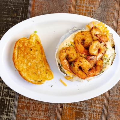 Baked potato topped with grilled shrimp, served with a slice of toasted bread.