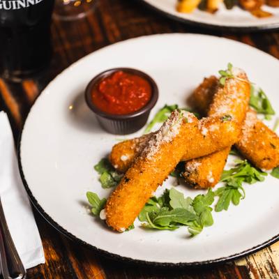 Mozzarella sticks served on a bed of arugula with a cup of marinara sauce.