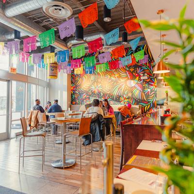 People dining in a bright restaurant with colorful banners and wall mural.