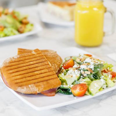 Grilled panini sandwich with fresh garden salad and feta cheese, served with orange juice.