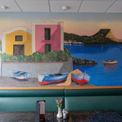 Colorful seaside mural above restaurant booth seating.