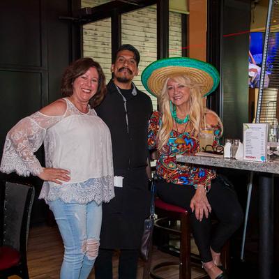 Three cheerful people, posing at a tall table, with one of them wearing a sombrero.