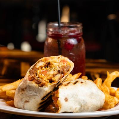 Buffalo Ranch Chicken Wrap with fries and a red cocktail on a table.