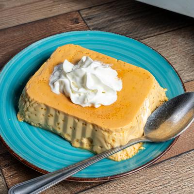 Flan topped with whipped cream on a blue plate with a spoon.