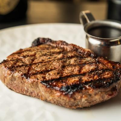 Grilled strip steak with a cup of sauce on a white plate.