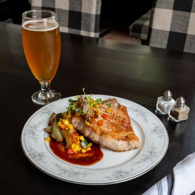 Pan-seared pork chop dish served with a vegetable medley and a side of beer.