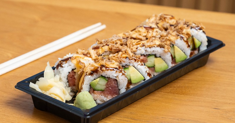 Sushi roll filled with tuna, avocado, and cucumber, topped with crispy fried onions