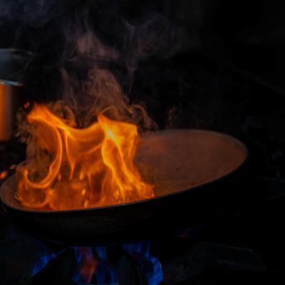 Frying pan on a stove with active flames rising from the cooking contents.