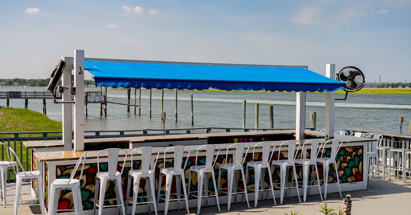 Outdoor bar with blue canopy and white stools by the waterfront