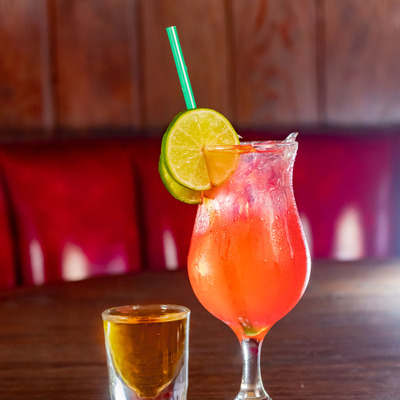 A shot glass and an orange cocktail with a lime wedge and a straw
