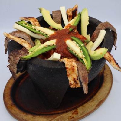 Molcajete dish with steak, chicken, jalapenos and avocado.