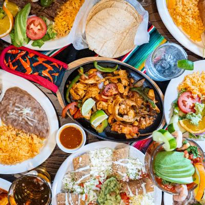 Mexican feast with chicken fajitas, rice, refried beans, tortillas, and drinks.