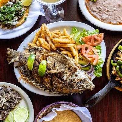 Whole fried Mojarra garnished with lime wedges, served with fries and a salad.