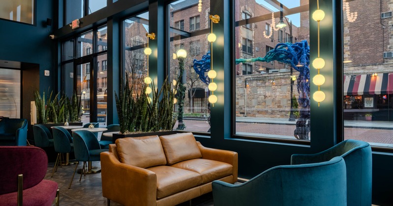 Interior seating area with a brown leather sofa, teal chairs, and decorative lighting