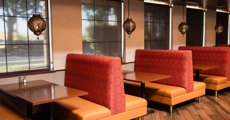 Restaurant interior with red and orange booths, wooden tables, hanging lamps, and large windows