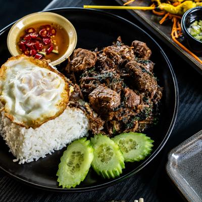 Ga Prao Braised Beef served with fried egg, rice, sliced cucumber and a sauce.
