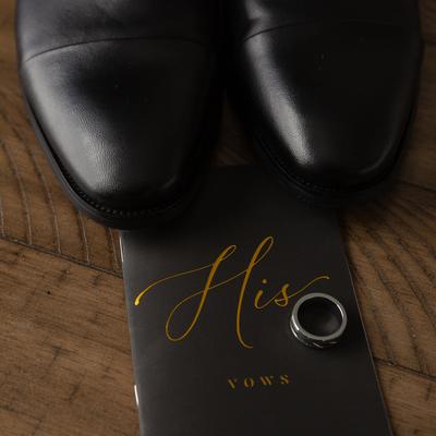 Black leather shoes and a ring placed on a groom's wedding vow book, top view, close up