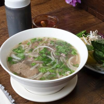Bolw of beef Pho served on the table with sides and condiments.