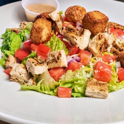 A chicken salad with lettuce, tomato, croutons and grated cheese..