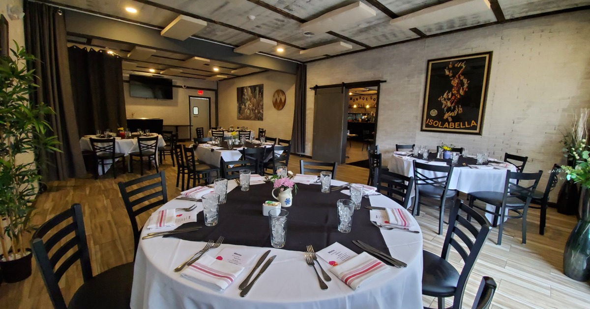 Elegant dining room with round tables set for guests, featuring white tablecloths and black napkins