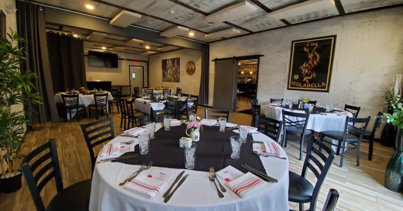Elegant dining room with round tables set for guests, featuring white tablecloths and black napkins