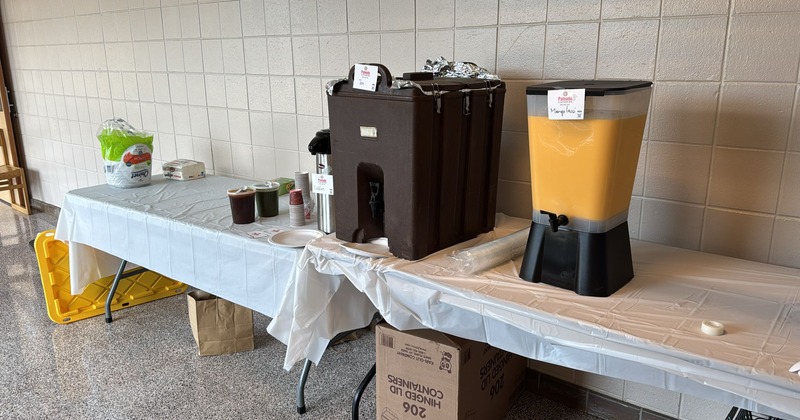 A table by a wall with Mango Lassi and Tea dispenser on it