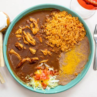 Chicken in mole sauce served alongside Mexican rice, refried 'beans, and salad.