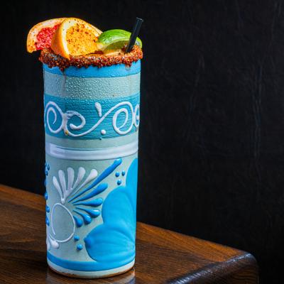 Mexican-style cocktail in a handcrafted blue glass with chili rim and citrus garnish.