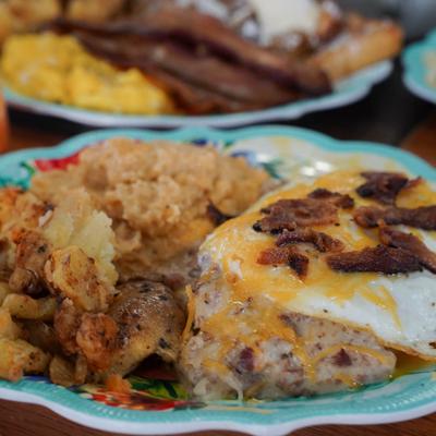 A plate featuring grits, smashed potatoes, and a fried egg toped with cheese and bacon.