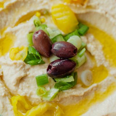 Hummus garnished with banana peppers, olives, green onions and olive oil.